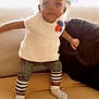 baby, bright_background, child, child_playing, child_wearing_socks, couch, cushion, furniture, home, indoor, indoor_lighting, living_room, motion_blur, overexposed, patterned_leggings, person, small_child, soft_toys, standing, white_top