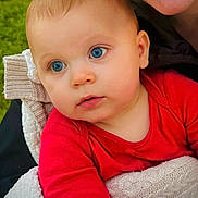 Warren is registered to the contest to win money with this photo: baby, child, blue_eyes, red_clothing, blanket, knit, face, smile, person, cuddle, portrait, outdoor, close_up, infant, young_child, happy, skin, head, warm, soft_texture