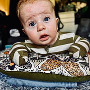 Logan joined the competition — help win amazing prizes! baby, infant, face, wide_eyes, striped_clothing, pillow, patterned_fabric, mittens, expression, curious, indoor, close_up, portrait, child, person, soft_lighting, couch, blanket, cute, home