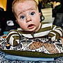 baby, infant, face, wide_eyes, striped_clothing, pillow, patterned_fabric, mittens, expression, curious, indoor, close_up, portrait, child, person, soft_lighting, couch, blanket, cute, home