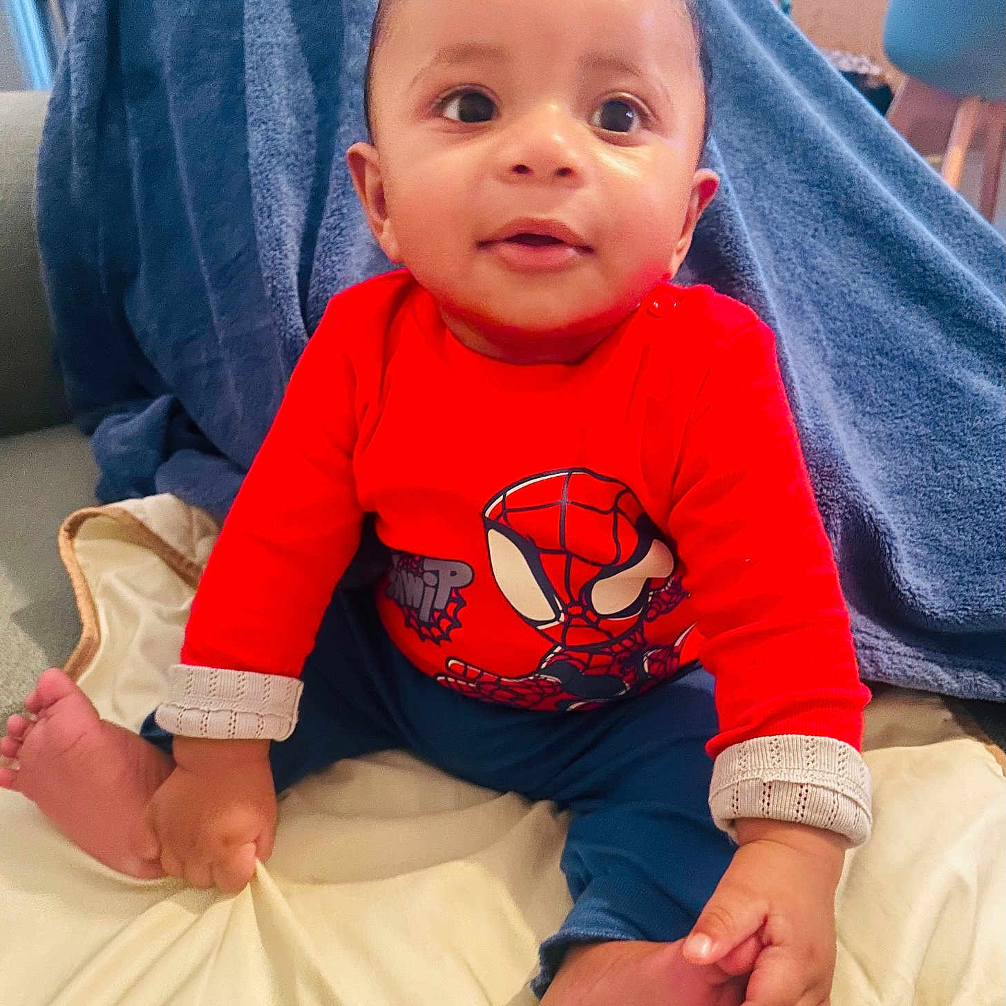 Ilyas participe au concours pour gagner de l'argent avec cette photo : baby, child, infant, red_shirt, spiderman, blue_pants, blanket, foot, hand, face, eyes, smile, indoor, furniture, towel, person, cute, portrait, sitting, cozy