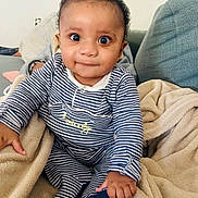 Ilyas a rejoint le concours — aidez-le/la à gagner de superbes lots ! baby, infant, striped_clothing, onesie, blanket, couch, indoor, child, smiling, curious, face, hand, foot, seated, soft_texture, home, cozy, cute, person, portrait