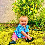 Jaxon Dean is registered to the contest to win money with this photo: baby, child, outdoor, grass, greenery, plant, yellow_flower, blanket, blue_shirt, pink_shorts, shoes, smiling, happy, sitting, cute, nature, portrait, young_child, sunlight, garden