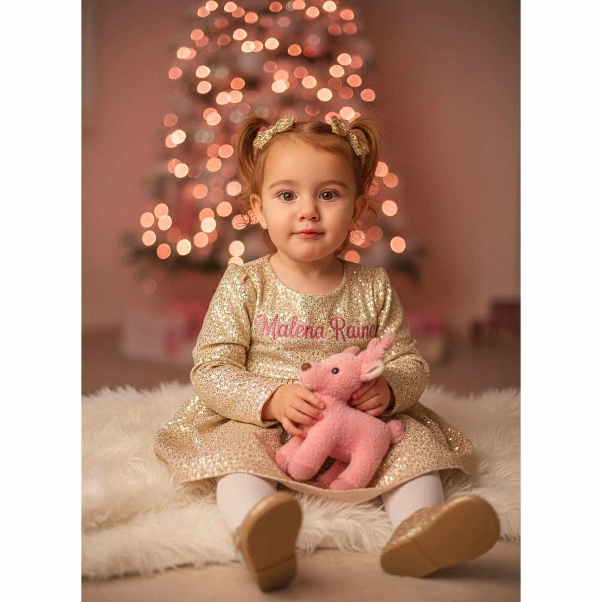 Malena joined the competition — help win amazing prizes! bokeh, bows, carpet, child, cute, festive, girl, gold_dress, gold_shoes, holiday_lights, indoor, pink_reindeer, plush_toy, pony_tail, portrait, smiling, soft_toy, toddler, warm_lighting, white_tights