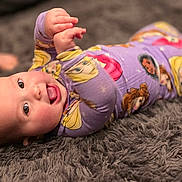 Aurora joined the competition — help win amazing prizes! baby, infant, pajamas, purple_clothing, princess_print, carpet, gray_rug, tongue_out, happy, smiling, lying_down, child, cute, indoor, soft_texture, person, closeup, playful, young_child, face