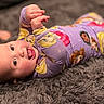 baby, infant, pajamas, purple_clothing, princess_print, carpet, gray_rug, tongue_out, happy, smiling, lying_down, child, cute, indoor, soft_texture, person, closeup, playful, young_child, face