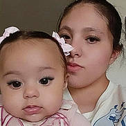 Selena is registered to the contest to win money with this photo: baby, child, woman, face, portrait, closeup, eyelashes, hair_bow, pink_clothing, casual_wear, indoor, skin, person, mother_and_child, young, expressionless, selfie, head_and_shoulders, cute, family