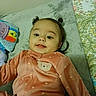 baby, child, infant, pigtails, pink_onesie, bear_patch, blanket, toy, smile, face, indoor, bed, patterned_bedding, cozy, cute, lying_down, soft_texture, home, childhood, happy