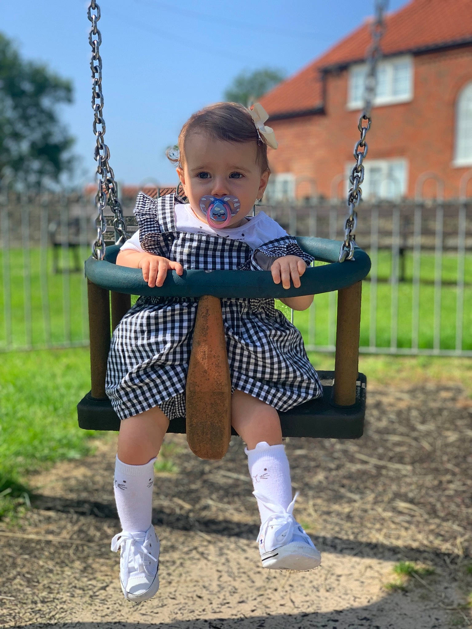 Effie is registered to the contest to win money with this photo: baby, child, city, design, human_settlement, knee, leg, outdoor_play_equipment, pattern, person, plaid, play, playground, public_space, recreation, sitting, swing, tartan, toddler, tree