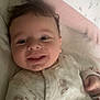 baby, infant, smiling, face, curly_hair, onesie, lion_print, bed, pillow, floral_pattern, blanket, child, cute, happy, lying_down, indoors, soft_light, person, comfort, cozy