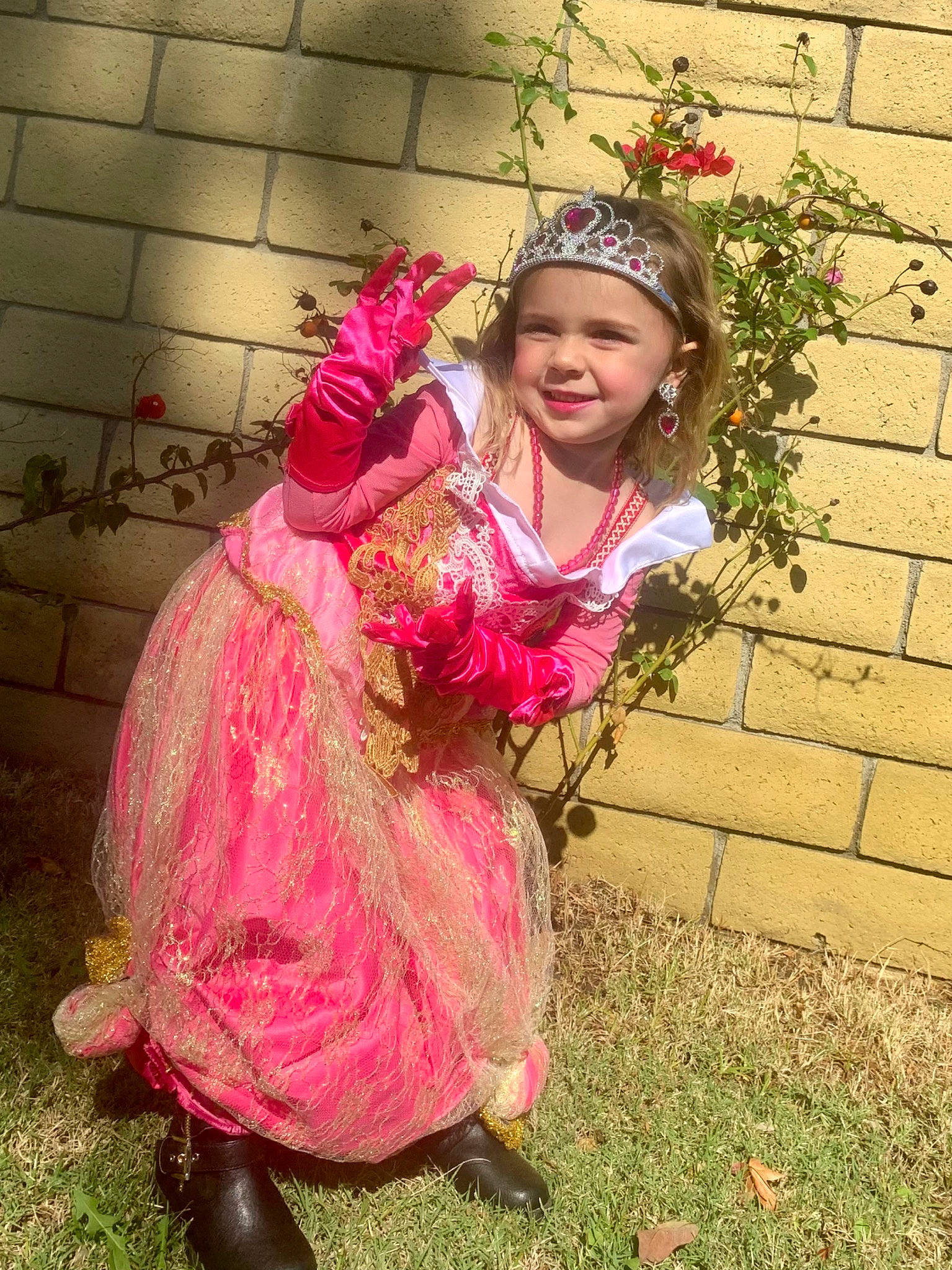 Keira is registered to the contest to win money with this photo: brick, child, costume, event, fun, grass, happy, headgear, headpiece, headwear, jewellery, joy, magenta, necklace, people_in_nature, person, pink, plant, sitting, smile