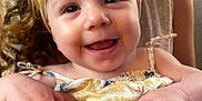 Sophia is registered to the contest to win money with this photo: baby, child, smile, happy, headband, bow, curly_hair, hands, holding, person, indoor, skin, face, clothing, sleeveless, cute, toddler, portrait, closeup, infant
