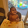 baby, high_chair, messy, food, smiling, face, hands, indoor, window, play_area, child, happy, tray, skin, mouth, seat, furniture, daylight, expression, young