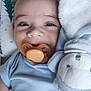 baby, pacifier, smile, blue_clothing, plush_toy, soft_texture, close_up, infant, cute, happy, indoors, child, head, face, comfort, cuddle, sleeping_bed, pillow, young, adorable