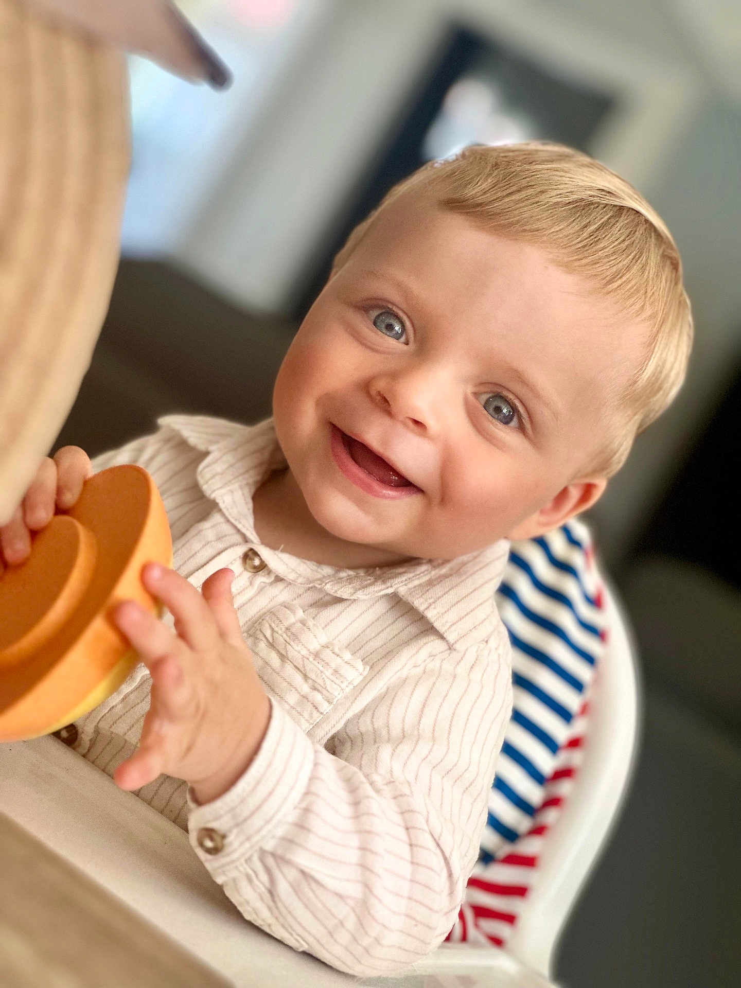 Lucas a rejoint le concours — aidez-le/la à gagner de superbes lots ! toddler, child, smiling, blue_eyes, blond_hair, striped_shirt, high_chair, toy, orange_toy, happy, indoors, portrait, baby, cute, infant, person, face, hand, seated, casual