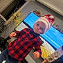 child, toddler, santa_hat, plaid_shirt, bow_tie, living_room, television, fairy_lights, holiday_decor, festive, standing, person, indoor, furniture, smile, hand, watching_tv, celebration, decorations, family