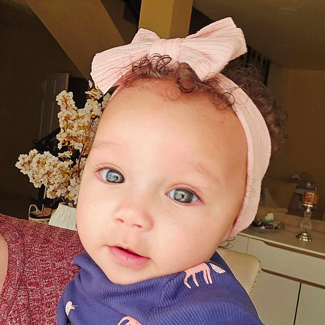 Reya is registered to the contest to win money with this photo: animal_print, baby, blue_eyes, bow, child, closeup, curly_hair, cute, face, flower, furniture, headband, home, indoor, person, portrait, purple_clothing, smiling, soft_lighting, toddler