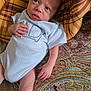 baby, infant, child, blue_onesie, elephant_embroidery, patterned_quilt, plaid_cushion, fabric, bed, hand, face, head, skin, lying_down, looking_away, indoors, soft_light, closeup, cute, portrait