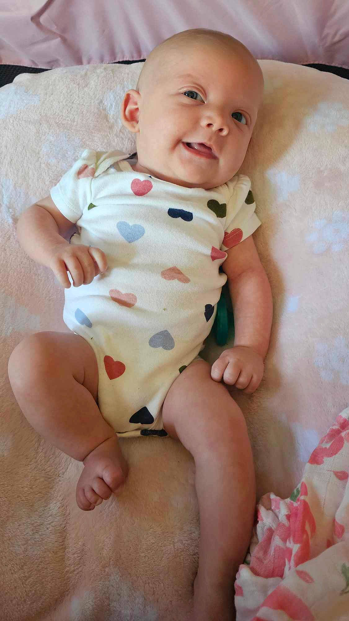 Harper is registered to the contest to win money with this photo: baby, baby_toddler_clothing, cheek, child, collar, comfort, eye, finger, human_leg, iris, leg, pattern, person, pink, sitting, skin, sleeve, smile, stomach, thumb