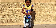 Christopher joined the competition — help win amazing prizes! black_hair, black_shoes, boy, brick_wall, child, daylight, football_helmet, football_uniform, happy, holding, outdoor, portrait, shadow, sidewalk, smile, sports_drink, standing, sunlight, white_pants, yellow_jersey