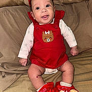 My Ari is registered to the contest to win money with this photo: baby, infant, smiling, red_overalls, christmas_slippers, reindeer_patch, bed, blanket, cute, happy, indoor, clothing, person, child, holiday, festive, apparel, footwear, sitting, portrait