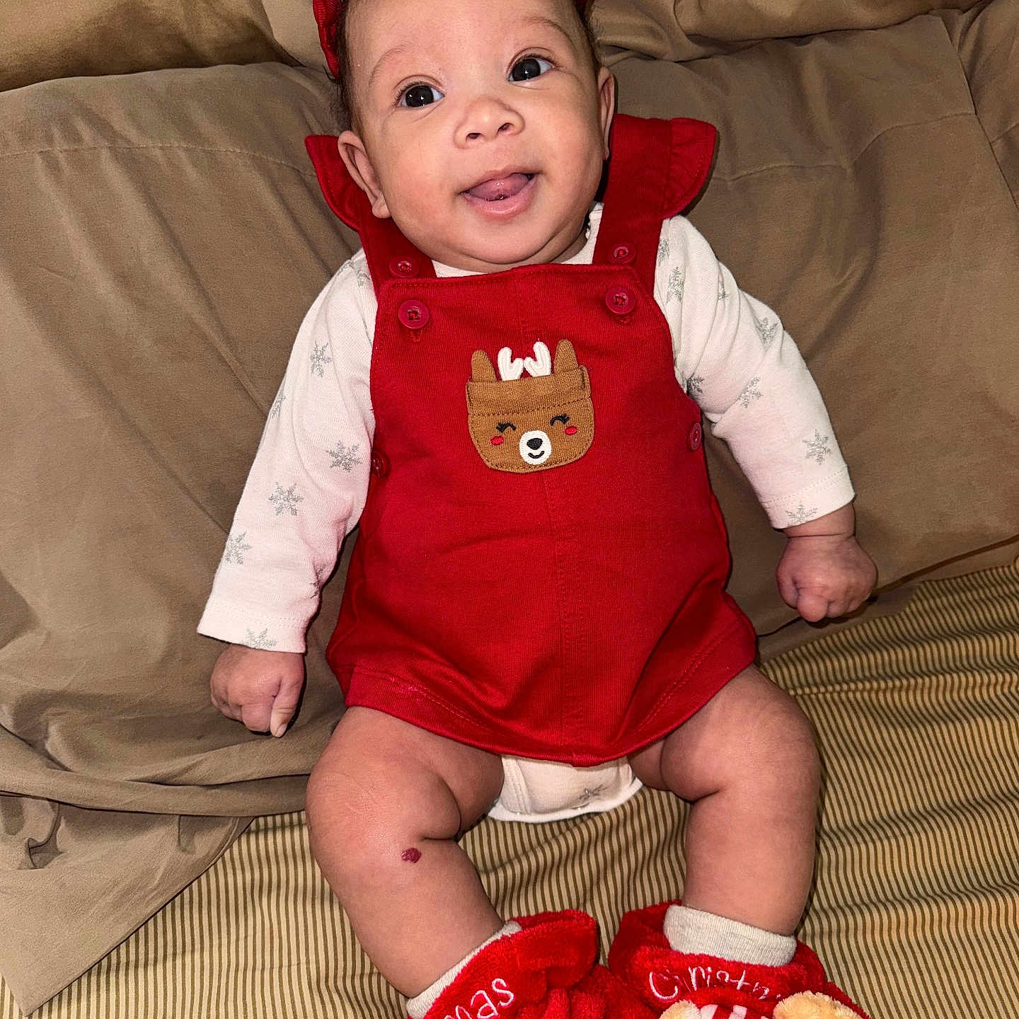 My Ari is registered to the contest to win money with this photo: apparel, baby, bed, blanket, child, christmas_slippers, clothing, cute, festive, footwear, happy, holiday, indoor, infant, person, portrait, red_overalls, reindeer_patch, sitting, smiling