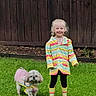 child, dog, grass, raincoat, boots, outdoor, fence, pet, playful, smiling, colorful, matching_outfits, happy, canine, lawn, young, casual, person, animal, weather
