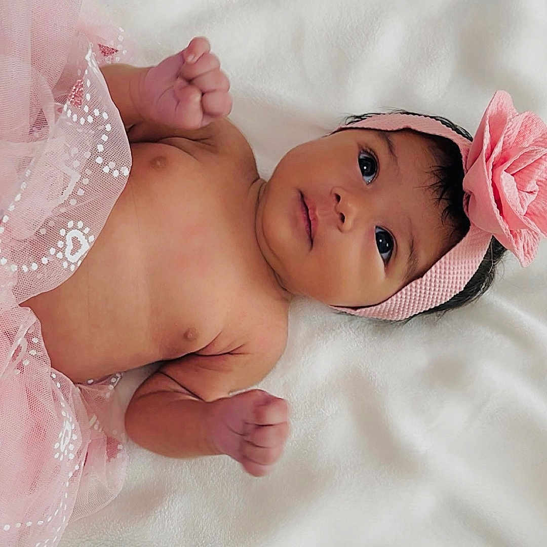 Delilah joined the competition — help win amazing prizes! baby, infant, headband, pink_flower, tulle_skirt, blanket, cute, lying_down, newborn, face, skin, hands, portrait, soft_texture, indoor, adorable, child, young, resting, curious