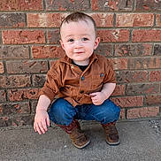 Hendrix is registered to the contest to win money with this photo: boy, brick_wall, casual_clothing, child, concrete, cowboy_boots, curly_hair, cute, daylight, fashion, front_view, jacket, jeans, outdoor, person, portrait, smiling, squatting, toddler, young_child