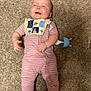 baby, infant, carpet, pink_onesie, bib, smiling, happy, footwear, indoor, toy, child, person, skin, face, head, clothing, caucasian, baby_shoes, lying_down, playful