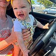 Avery joined the competition — help win amazing prizes! baby, child, yellow_bow, steering_wheel, car_interior, smiling, young_man, hand, sunlight, clothing, seat, window, outdoor, daylight, portrait, playful, happy, person, holding, vehicle