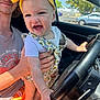 baby, child, yellow_bow, steering_wheel, car_interior, smiling, young_man, hand, sunlight, clothing, seat, window, outdoor, daylight, portrait, playful, happy, person, holding, vehicle