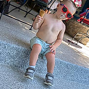 Ariakus is registered to the contest to win money with this photo: toddler, child, ice_cream, sunglasses, summer, outdoor, steps, casual_clothing, shorts, bare_chest, footwear, sneakers, sunny, messy_face, playful, relaxed, daytime, shaded_area, fun, cute