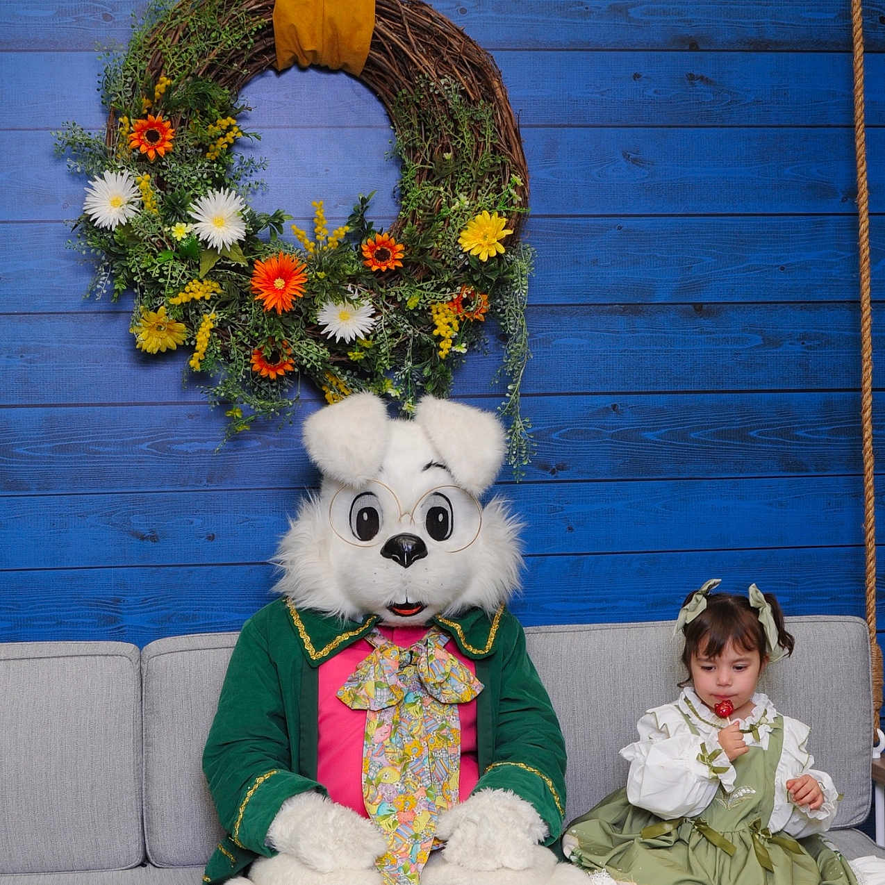 Saige joined the competition — help win amazing prizes! blue_wall, child, costume, couch, cute, decoration, eating, flowers, glasses, green_dress, holiday, indoor, lollipop, person, playful, ribbon, sitting, toy, white_fur, wreath
