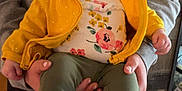 Zara is registered to the contest to win money with this photo: baby, child, infant, yellow_headwrap, yellow_jacket, floral_onesie, green_pants, white_slippers, hands, person_holding, indoor, wooden_floor, gray_sweatshirt, nike_logo, cute, portrait, cozy, soft_slippers, casual_clothing, calm_expression