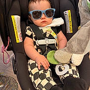 Kasin is registered to the contest to win money with this photo: baby, infant, child, car_seat, sunglasses, serious_expression, portrait, sitting, harness, blanket, stuffed_toy, pacifier, indoor, home, clothing, black_and_white_outfit, toy, face, photography, funny