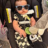 baby, infant, child, car_seat, sunglasses, serious_expression, portrait, sitting, harness, blanket, stuffed_toy, pacifier, indoor, home, clothing, black_and_white_outfit, toy, face, photography, funny