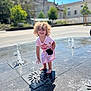 Mia a rejoint le concours — aidez-le/la à gagner de superbes lots ! child, curly_hair, smile, water_fountain, splash, barefoot, pink_dress, outdoor, sunny, plaza, playing, puddle, happy, candid, portrait, urban, building, church, bokeh, summer