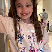 Mia participe au concours pour gagner de l'argent avec cette photo : child, girl, smile, pigtails, sweatshirt, cartoon_characters, indoor, hallway, doorway, long_hair, casual_pose, people_in_background, happy, young, childhood, portrait, clothing, bright, person, cute