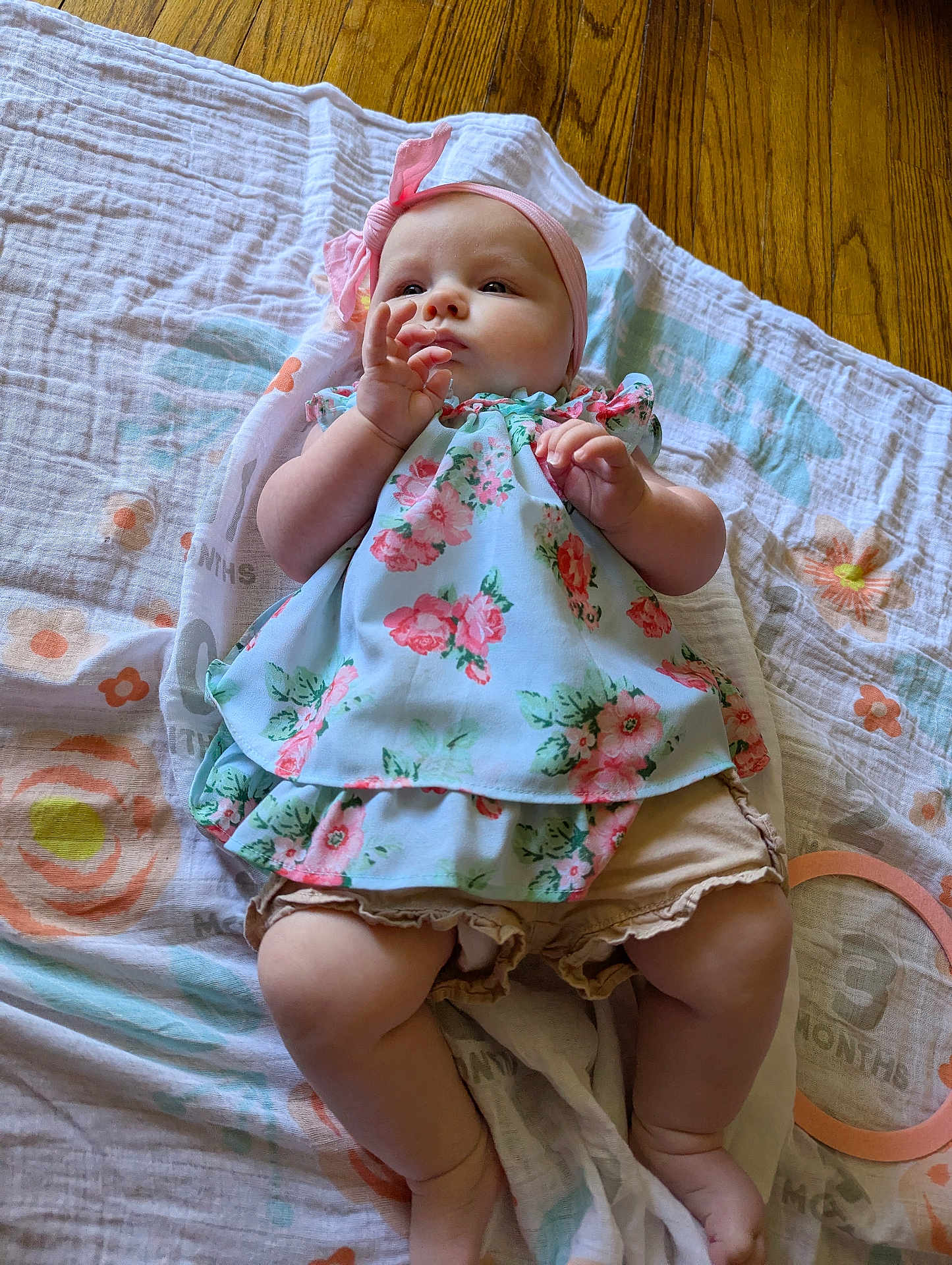 Abby joined the competition — help win amazing prizes! baby, infant, child, blanket, floor, wooden_floor, headband, bow, dress, floral_pattern, legs, hands, skin, cute, indoors, laying_down, person, apparel, soft_texture, natural_light