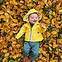 autumn_leaves, baby, baby_clothing, child, cute, fall, fall_colors, grass, green_pants, happy, infant, leaf, nature, outdoor, park, person, playful, seasonal, smiling, yellow_raincoat