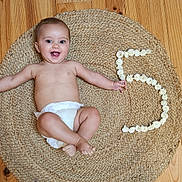 émile a rejoint le concours — aidez-le/la à gagner de superbes lots ! baby, diaper, smiling, happy, infant, floor, wooden_floor, rug, woven_rug, flowers, number_5, milestone, celebration, arms_outstretched, barefoot, indoor, child, cute, portrait, lying_down