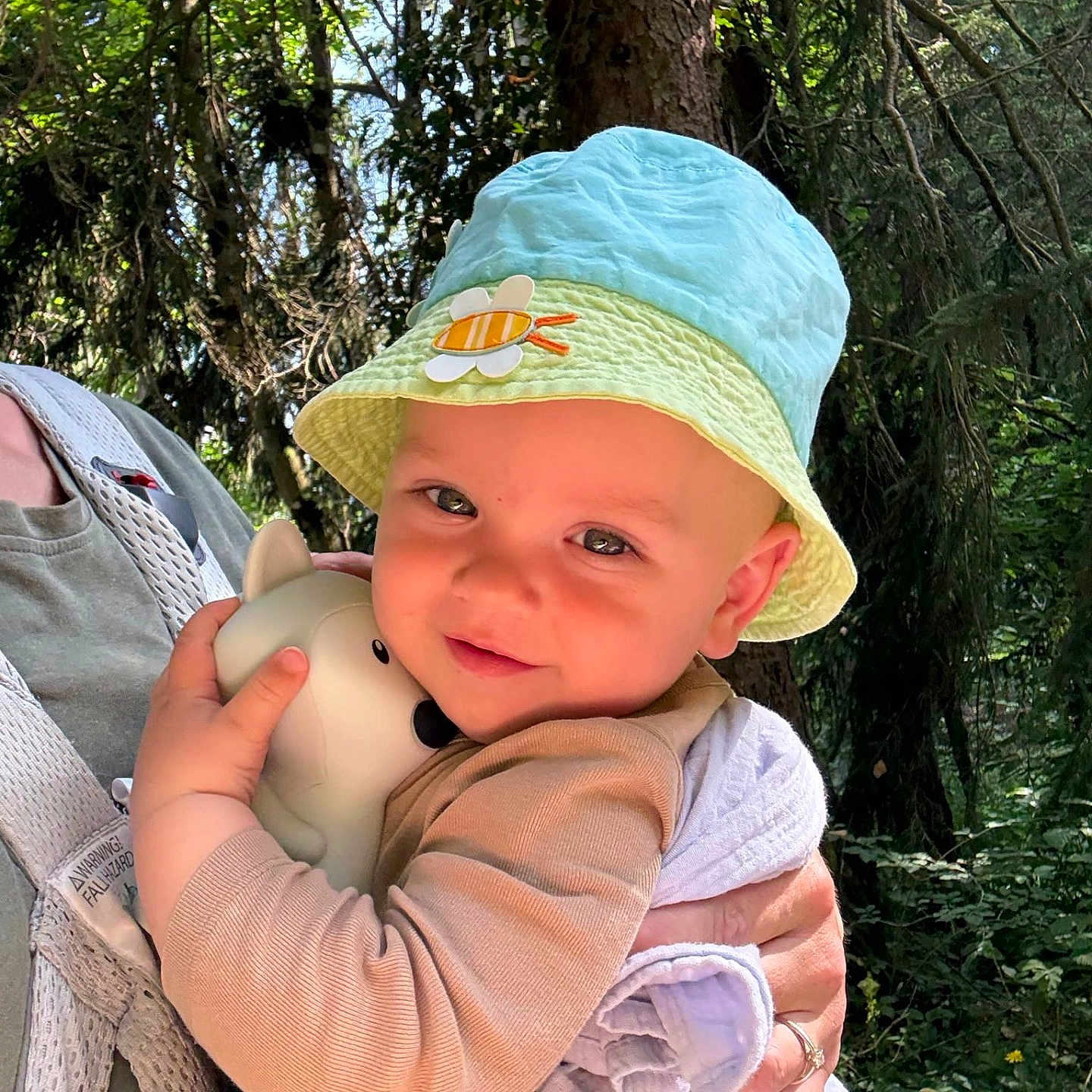 Félix a rejoint le concours — aidez-le/la à gagner de superbes lots ! adult, baby, child, clothing, cute, daylight, face, forest, greenery, hat, holding, hugging, infant, nature, outdoors, person, smiling, sunlight, toy, trees