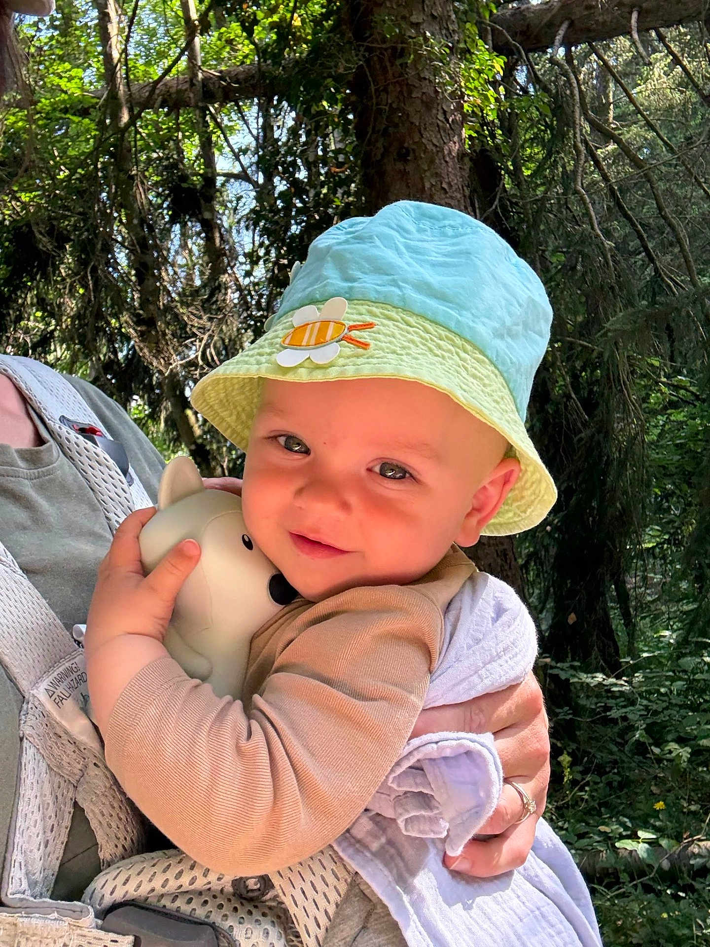 Félix a rejoint le concours — aidez-le/la à gagner de superbes lots ! baby, child, hat, toy, forest, nature, outdoors, person, hugging, sunlight, trees, greenery, cute, infant, holding, smiling, clothing, adult, daylight, face