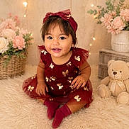 Elif is registered to the contest to win money with this photo: toddler, child, dress, headband, maroon, golden_bows, smiling, sitting, carpet, fluffy, teddy_bear, flowers, basket, indoor, cute, portrait, happy, baby, soft_lighting, decor