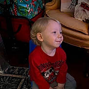 Luka is registered to the contest to win money with this photo: child, toddler, red_sweater, mickey_mouse, chair, indoor, holiday_bags, yellow_armchair, carpet, smile, blond_hair, casual_clothing, sneakers, floor, portrait, seated, furniture, home, festive, young_child
