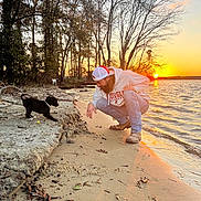 Boosie is registered to the contest to win money with this photo: sunset, beach, man, puppy, dog, water, sand, trees, nature, outdoor, sun, shore, casual_clothing, cap, sky, reflection, playful, animal, pet, landscape