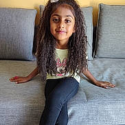 Evy participe au concours pour gagner de l'argent avec cette photo : black_leggings, casual_clothing, child, couch, cross_legged, curly_hair, flower_hair_accessory, girl, gray_couch, home, indoor, minnie_mouse, person, portrait, relaxed, sitting, smiling, tshirt, yellow_wall, young