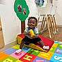 alphabet, bib, chair, child, daycare, decor, floor, happy, indoor, photograph, play, playmat, shorts, smiling, sock, toddler, toy, wall, wood, yellow
