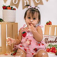Gabriella joined the competition — help win amazing prizes! baby, toddler, cake, birthday, messy, frosting, strawberry, pink_dress, child, celebration, smiling, crate, banner, food, party, cute, sitting, face, hands, first_birthday